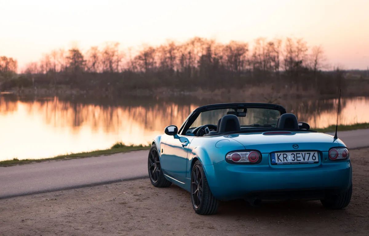 Niebieska Mazda MX-5 ze złożonym dachem nad jeziorem o zachodzie słońca