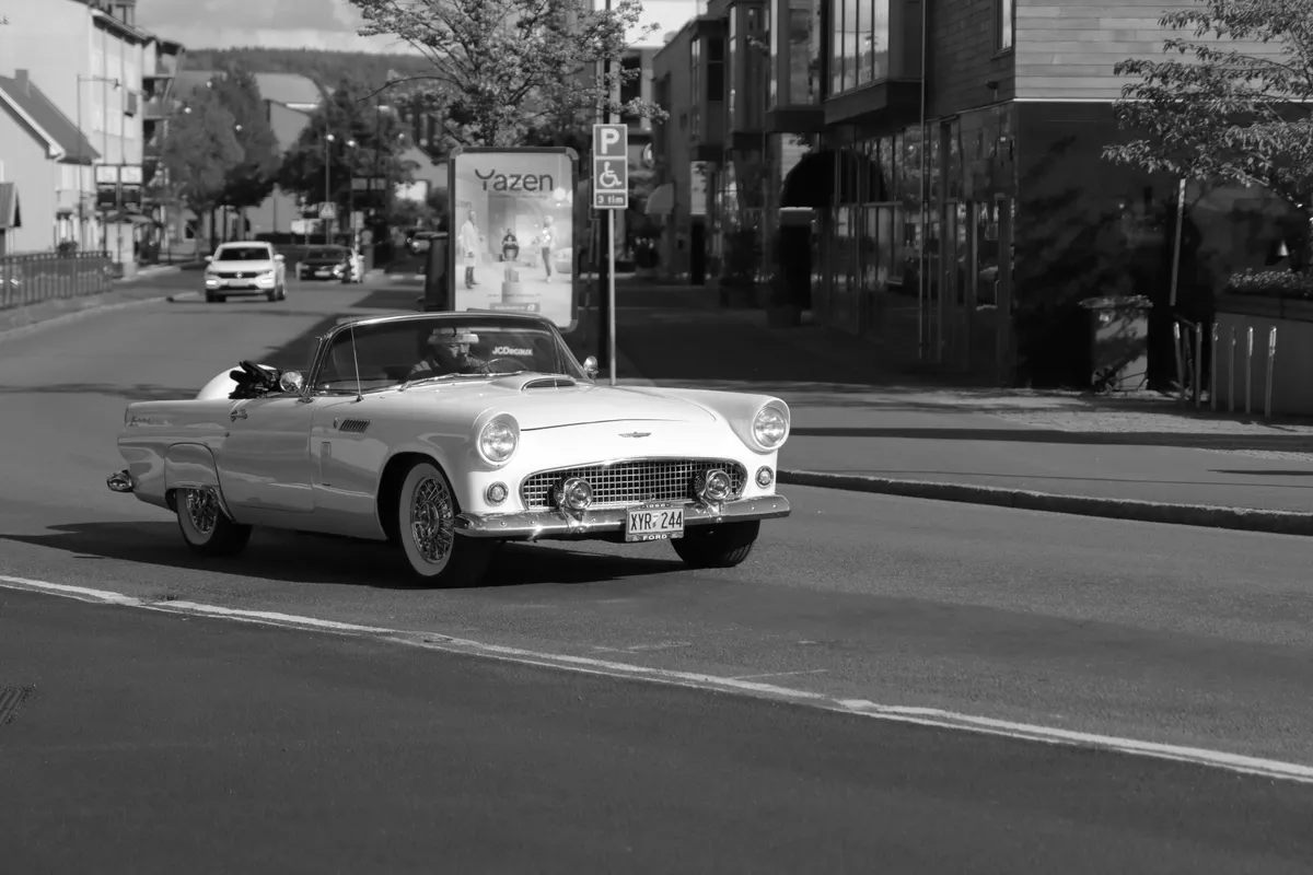 Czarno-białe zdjęcie klasycznego kabrioletu Ford Thunderbird jadącego ulicą miasta